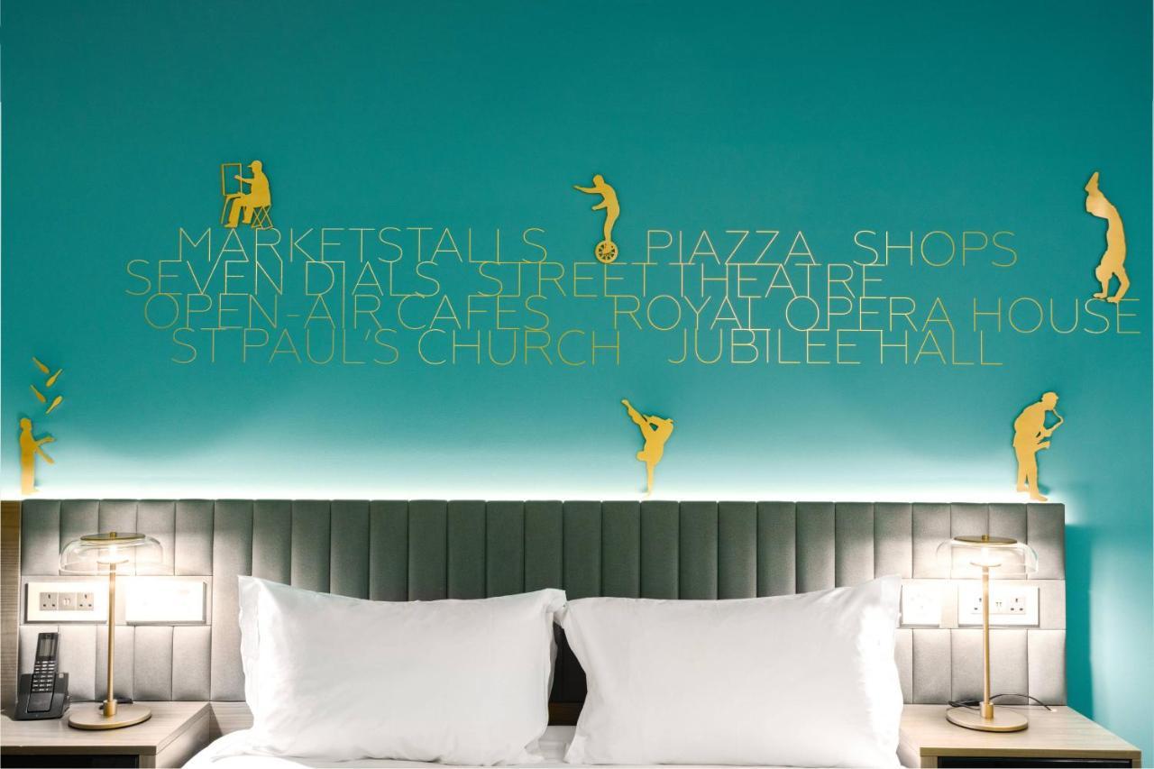 Middle Eight - Covent Garden - Preferred Hotels And Resorts London Bagian luar foto The photo shows a modern hotel room with a distinctive turquoise wall. On the wall, there are gold silhouettes of people engaged in various activities, suggesting movement or leisure. The wall also features text that highlights local attractions like