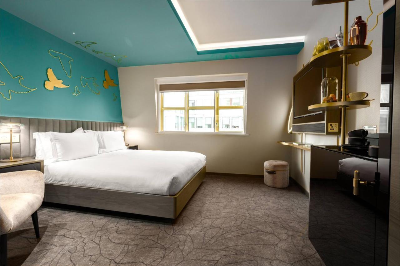 Middle Eight - Covent Garden - Preferred Hotels And Resorts London Bagian luar foto The photo shows a modern hotel room featuring a large bed with white linens positioned against a wall. The decor includes a striking turquoise ceiling and decorative elements, such as yellow motifs, on the wall. There are large windows allowing natur