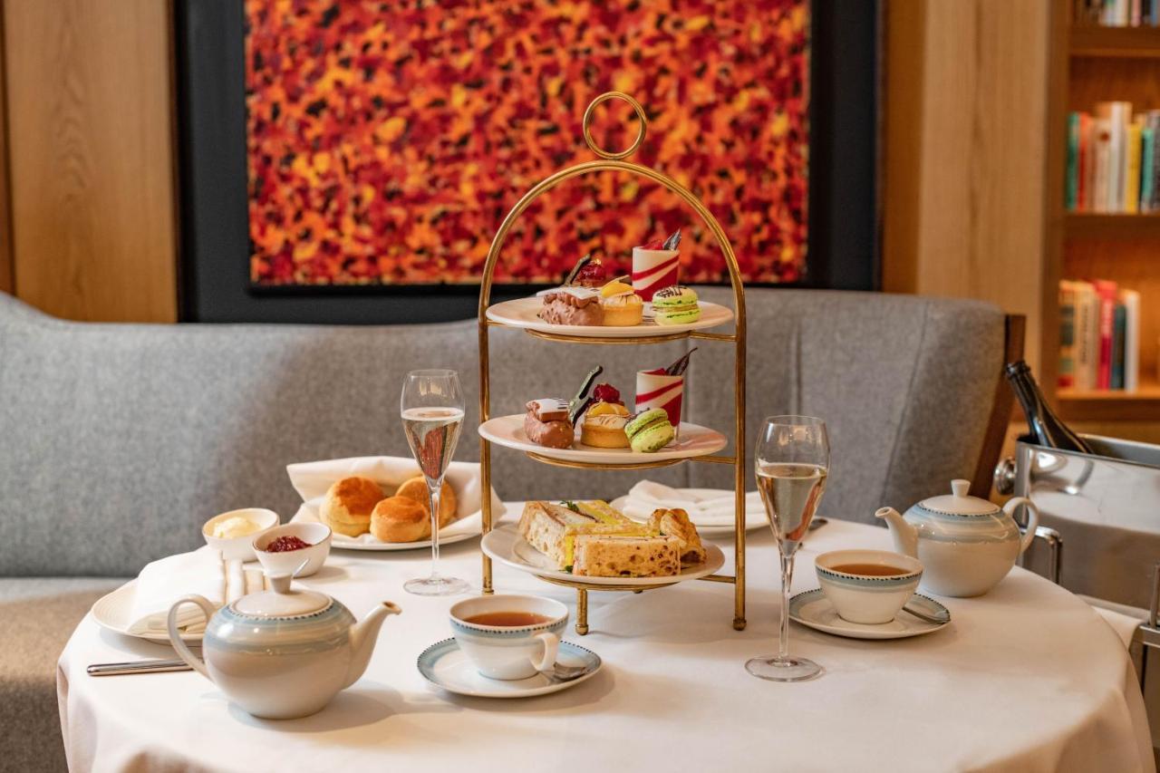 Middle Eight - Covent Garden - Preferred Hotels And Resorts London Bagian luar foto The photo shows an elegant afternoon tea setup on a white tablecloth. At the center, there is a multi-tiered stand displaying a variety of pastries and desserts, including cakes and colorful sweets. Surrounding the stand are teapots and teacups, read