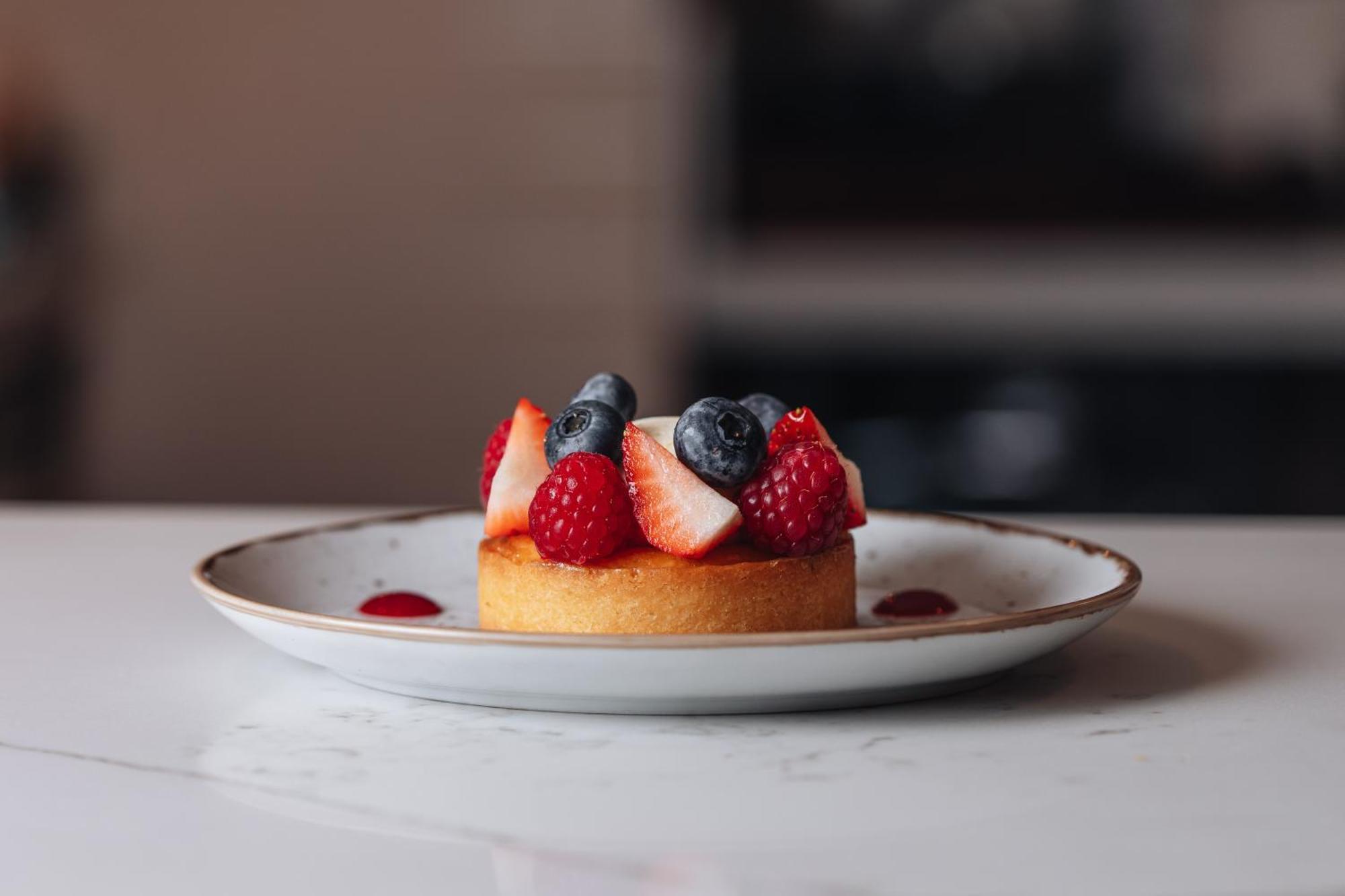 Middle Eight - Covent Garden - Preferred Hotels And Resorts London Bagian luar foto The photo shows a delicious-looking dessert on a white plate. The dessert appears to be a small tart or cake topped with fresh strawberries, raspberries, and blueberries. It has a golden crust, and there are small dollops of a red sauce or fruit pure