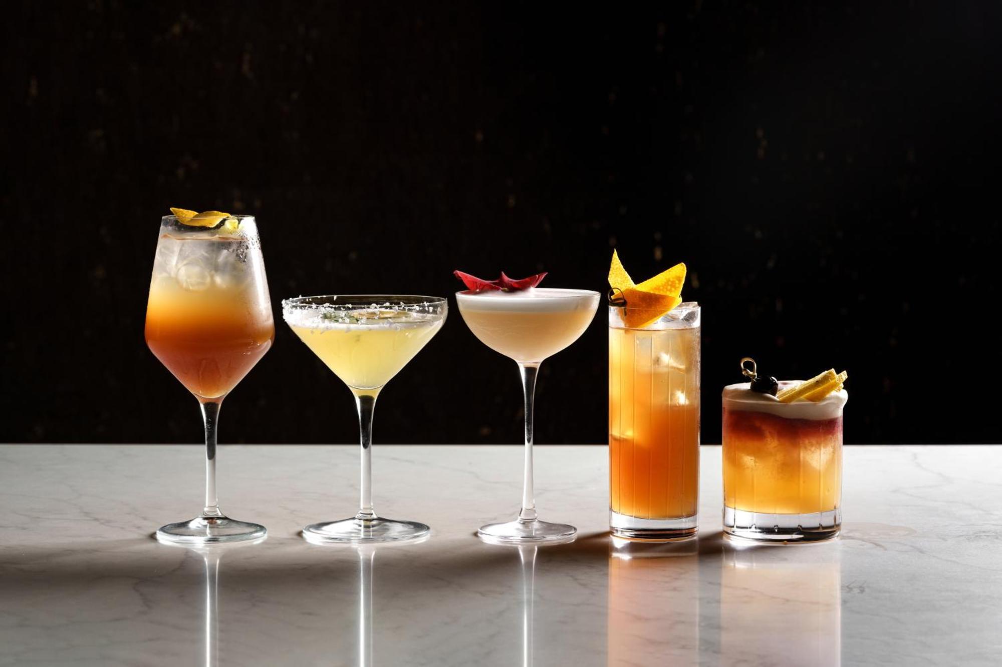 Middle Eight - Covent Garden - Preferred Hotels And Resorts London Bagian luar foto The photo features a selection of five different cocktails lined up on a marble surface. Each drink is served in a distinct glass, showcasing a variety of colors and garnishes. 

1. The first cocktail is in a large wine glass, with a gradient color f