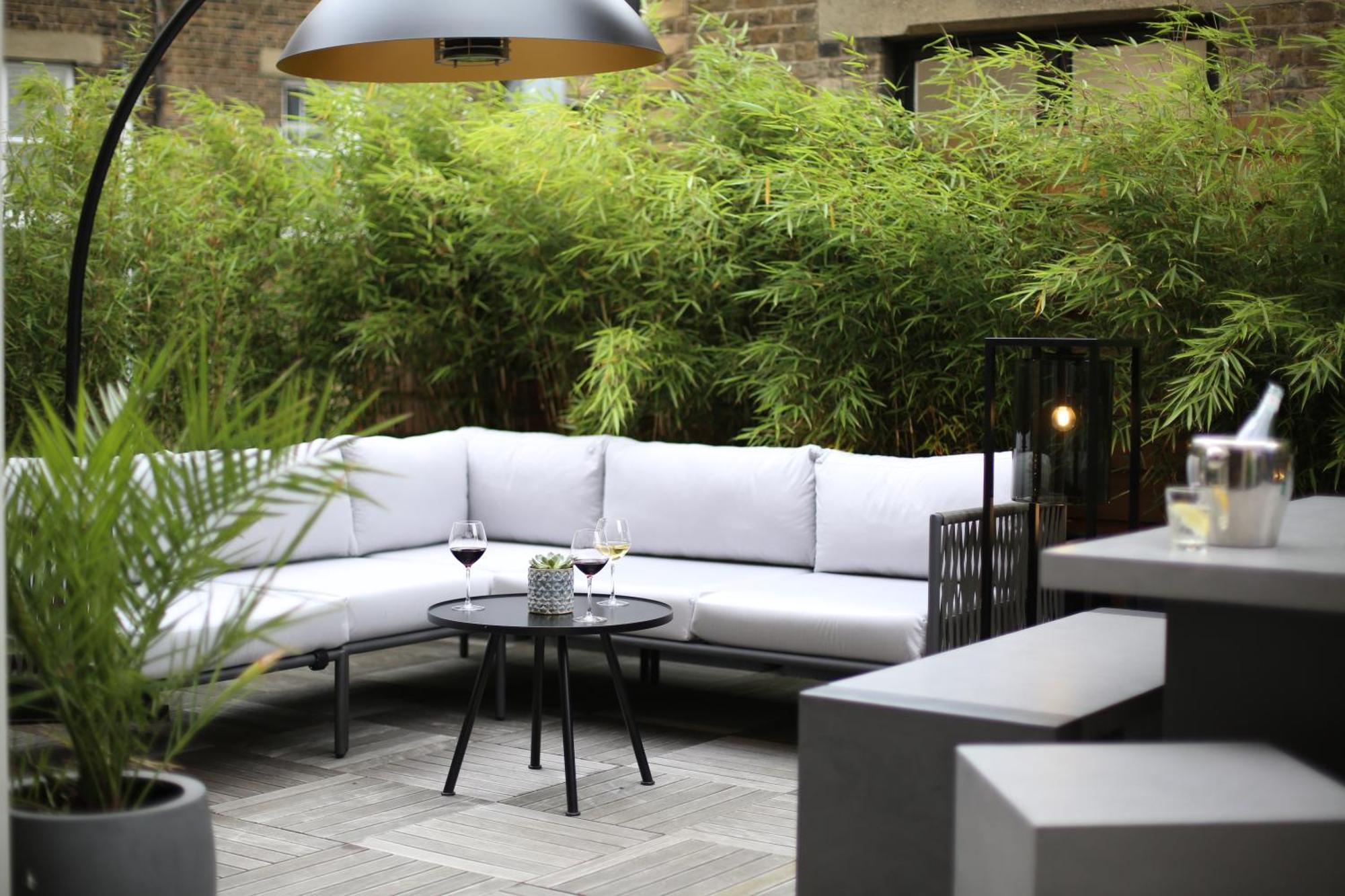 Middle Eight - Covent Garden - Preferred Hotels And Resorts London Bagian luar foto The photo shows an outdoor seating area featuring a modern gray sectional sofa with plush cushions. In front of the sofa is a small, round black table with two glasses of wine on it, accompanied by a decorative plant or vase. Surrounding the area are
